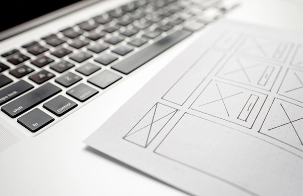 ノートPCと紙のワイヤーフレームのスケッチ